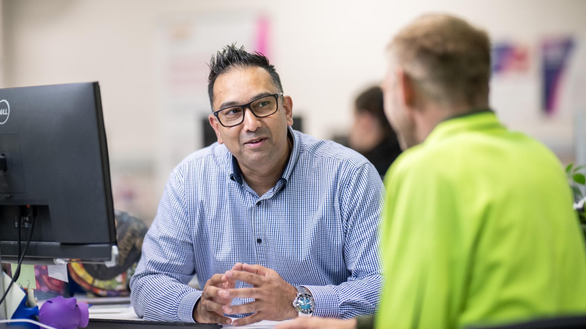 An APM consultant at a desk discussing Workforce Australia support with a participant.
