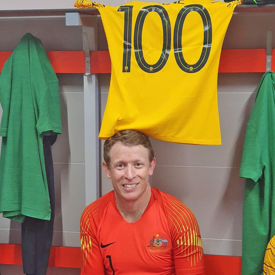 Chris Pyne smiling at the camera infront of a yellow jersey with 100 printed on the back