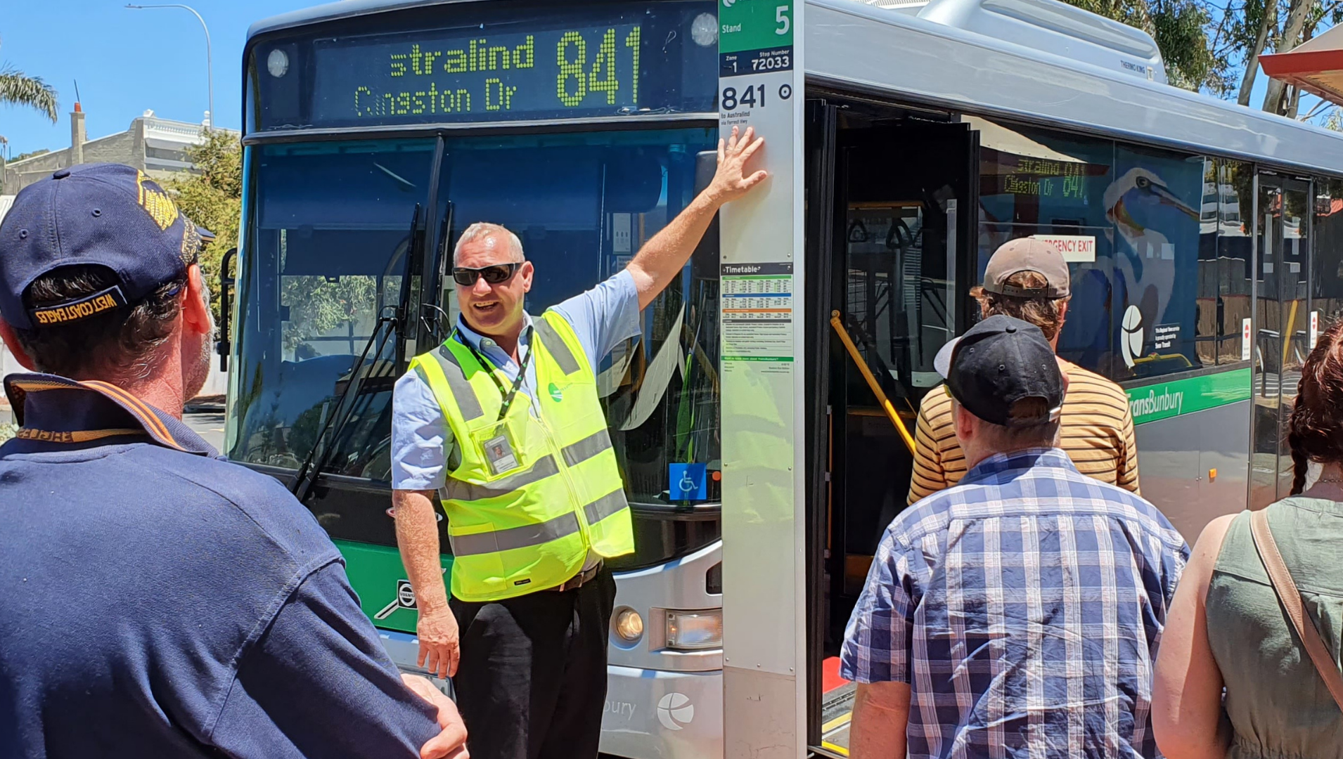 A Transperth worker showing a small crowd of people a stationary bus timetable